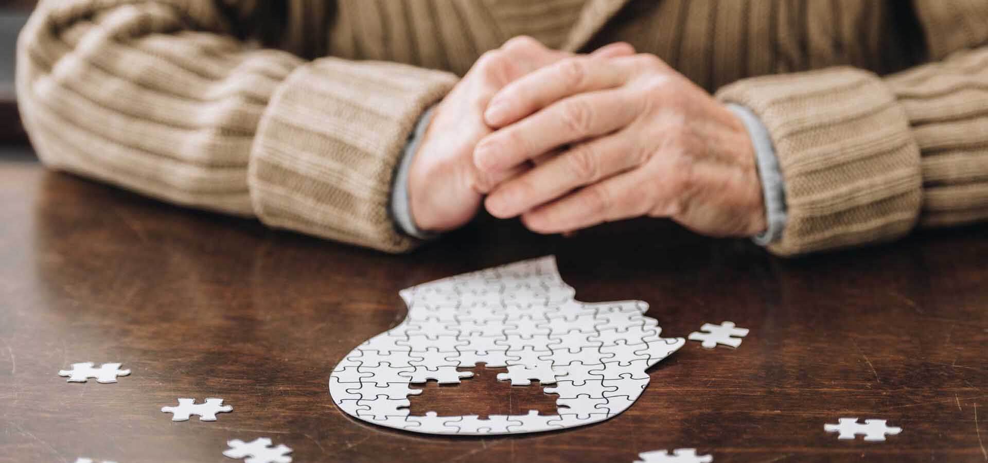 Hände eines älteren Mannes mit einem Puzzle in Form eines Kopfes